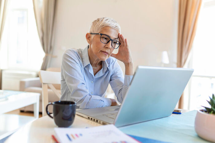 Older woman with glasses looking confused at a laptop, illustrating parents being bad at technology skills in a funny way.