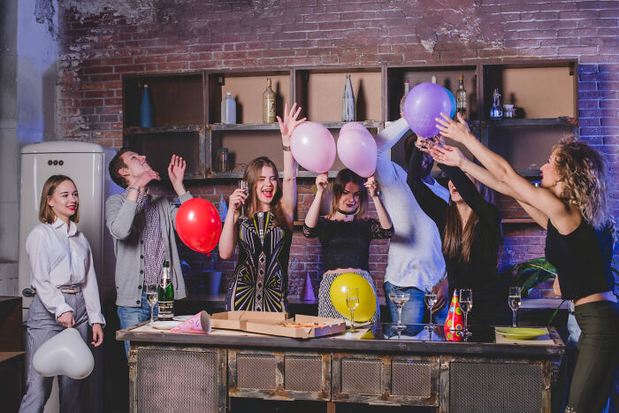 Group of young people celebrating with balloons and drinks indoors, illustrating shocking things popular kids did in school.