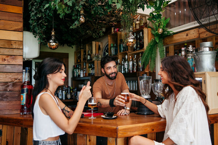 Restaurant staff serving drinks and interacting with customers in a lively bar setting before the bill arrives.