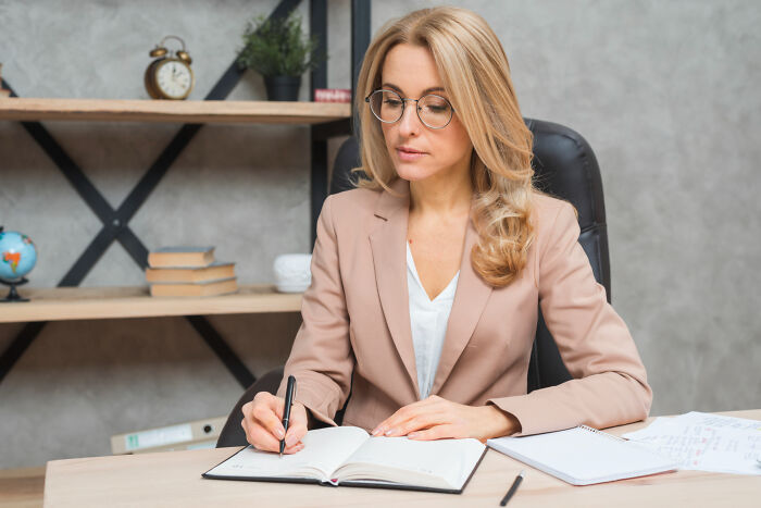 Woman in glasses and blazer writing in a notebook, illustrating unfair relationships influenced by gender roles.