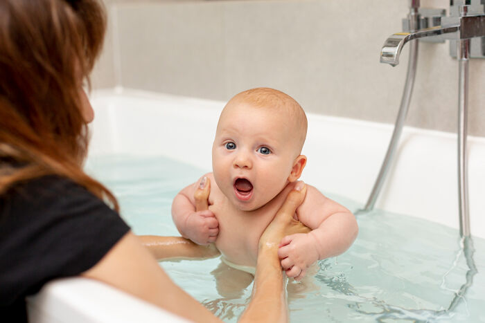 Baby with surprised expression in bathtub held by adult, illustrating unfair relationships influenced by gender roles.