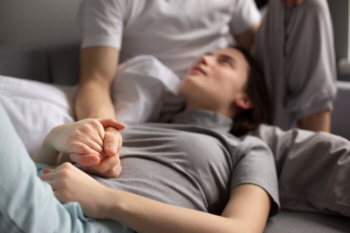 Person lying down holding hands with a supportive companion, highlighting terrifying medical conditions without symptoms.