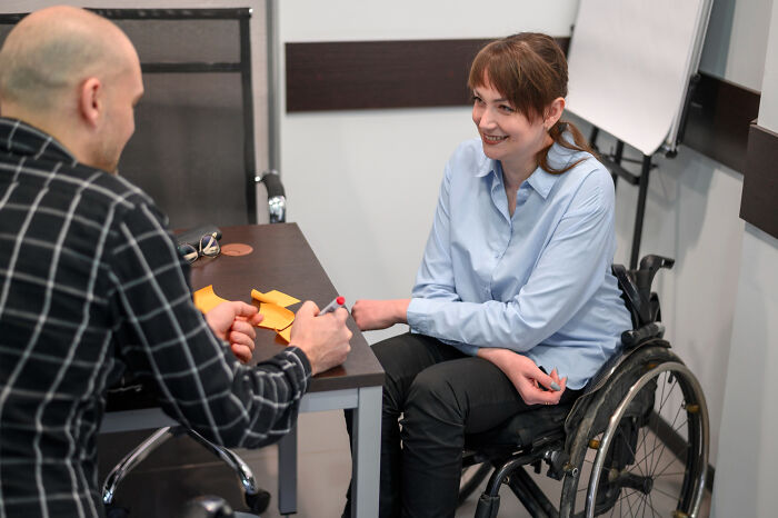A woman in a wheelchair talking with a man at a table, illustrating people with disabilities facing rude and ableist comments.