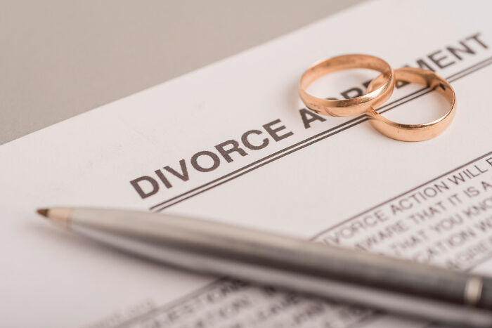 Two wedding rings on a divorce agreement document with a pen nearby symbolizing disturbing relationship realities.