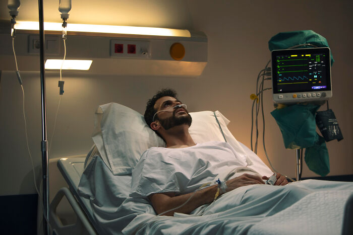 Man lying in a hospital bed connected to medical monitoring equipment, evoking scary ghost stories hospital work atmosphere.