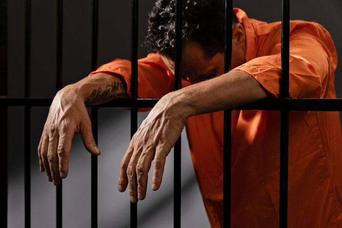 Man in orange prison uniform behind bars, symbolizing consequences when the bill comes and the money doesn’t pay.