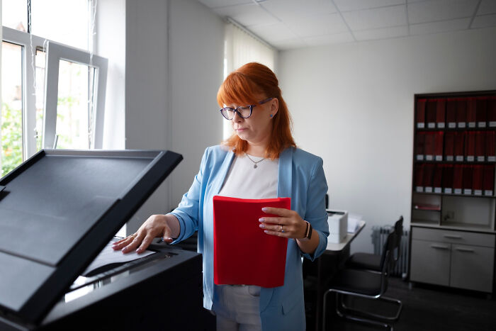 Woman with red folder using a photocopier in an office.