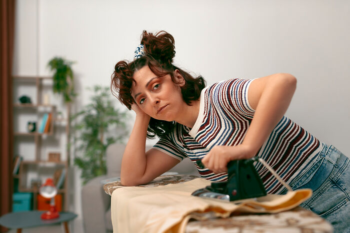 Young woman looking distressed while ironing clothes, illustrating unfair relationships affected by traditional gender roles.