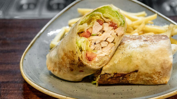 Grilled chicken wrap with lettuce and tomato, served with golden French fries on a gray plate.