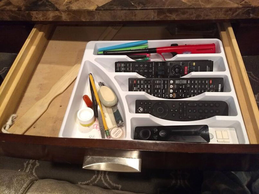 Drawer with multiple compartments neatly organizing remotes, pens, and small household items using organization hacks.