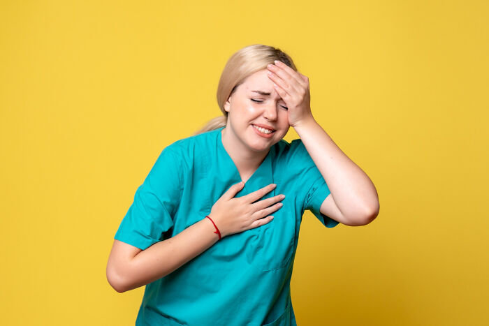 Woman in medical scrubs clutching chest and forehead in pain, illustrating terrifying medical conditions without symptoms.