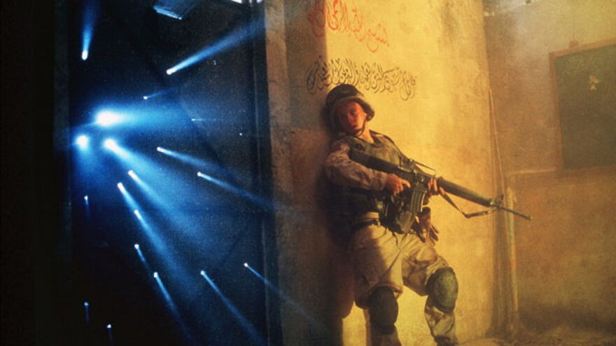 Soldier in combat gear holding a rifle, leaning against a wall with light beams in a movie scene based on true stories.