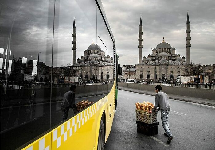 Boy pushing bread cart next to a yellow bus with a historic mosque in the background on Istanbul’s streets.