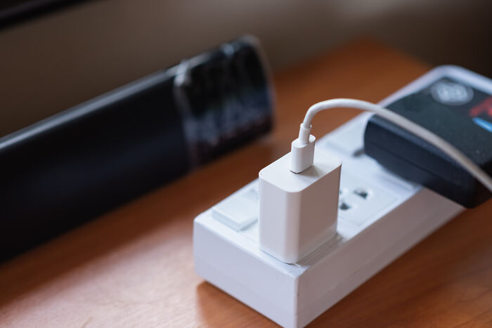 White phone charger plugged into a power strip on a wooden surface, illustrating common life hacks and tricks.