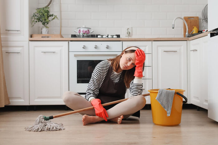 Woman wearing red gloves sitting on the floor with mop and bucket, depicting unfair relationships due to gender roles.