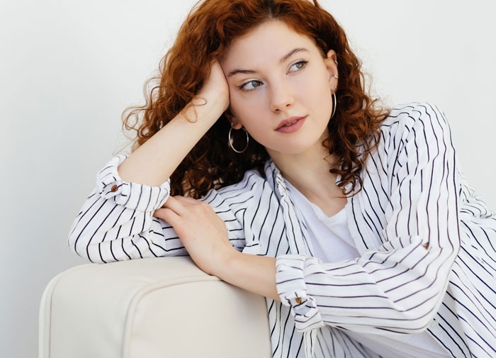 Young woman with curly hair in a striped shirt looking thoughtful, illustrating company claims on raises and new hire pay. Young woman with curly hair in a striped shirt looking thoughtful, illustrating company claims on raises and new hire pay.
