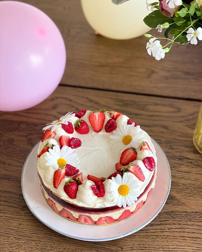 Strawberry and cream cake decorated with daisies on a wooden table with balloons and flowers nearby, teen cake fail theme. Strawberry and cream cake decorated with daisies on a wooden table with balloons and flowers nearby, teen cake fail theme.