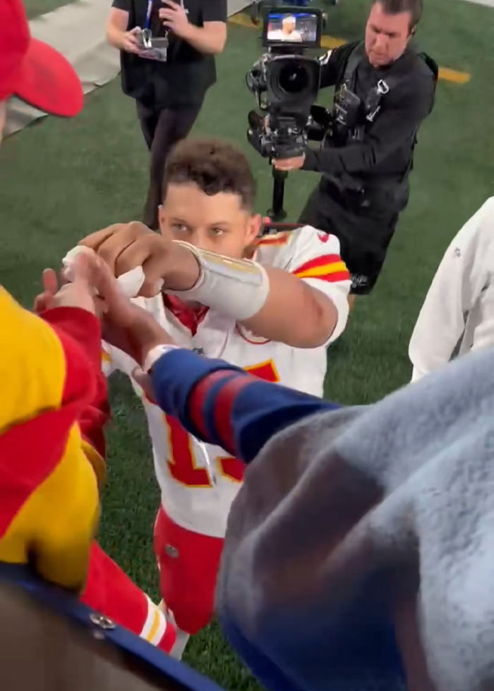 Football player on field with camera crew and fans, related to viral Kansas City Karen headband snatching incident. Football player on field with camera crew and fans, related to viral Kansas City Karen headband snatching incident.