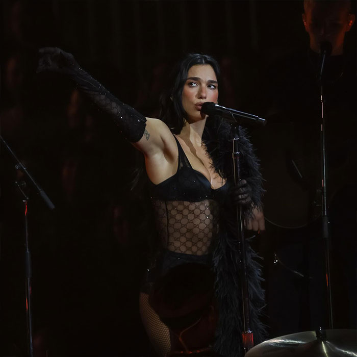 Dua Lipa performing in a concert wearing a black outfit, raising her arm as crowd reacts to viral video controversy. Dua Lipa performing in a concert wearing a black outfit, raising her arm as crowd reacts to viral video controversy.