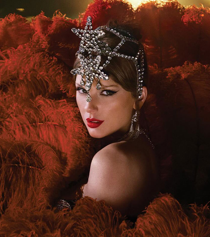 Taylor Swift wearing an ornate headpiece and red lipstick in a glamorous setting with red feathered background. Taylor Swift wearing an ornate headpiece and red lipstick in a glamorous setting with red feathered background.