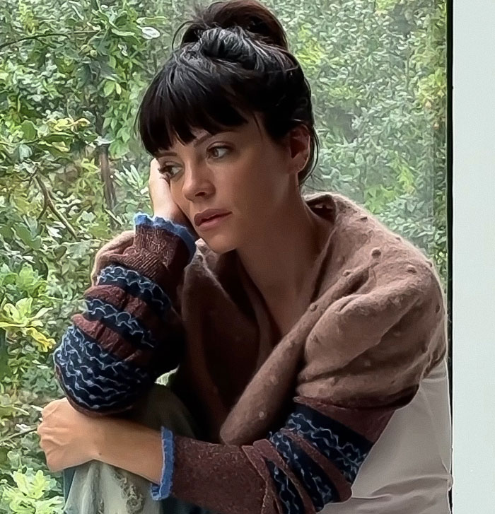 Woman with dark hair in a bun sitting by a window, appearing thoughtful amid discussions about David Harbour cheating controversy. Woman with dark hair in a bun sitting by a window, appearing thoughtful amid discussions about David Harbour cheating controversy.