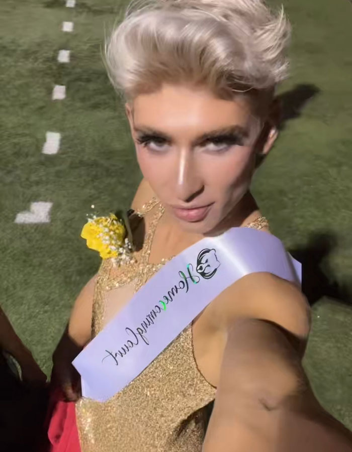 Young man wearing a gold dress and homecoming queen sash taking a selfie on a sports field after his viral win. Young man wearing a gold dress and homecoming queen sash taking a selfie on a sports field after his viral win.