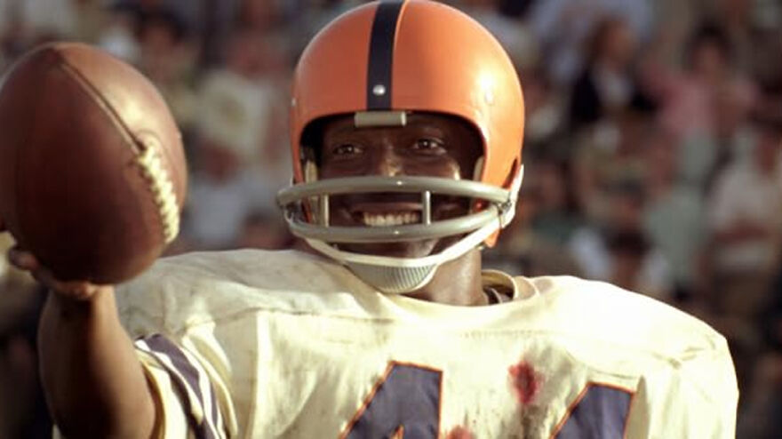 Actor in vintage football uniform and helmet holding ball, representing movies based on true stories that feel impossible to believe