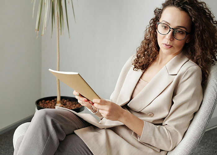 Woman with curly hair and glasses in a beige blazer reading a notebook, related to psychologists debunking mental health myths.