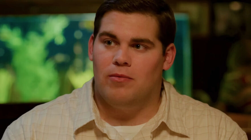 Young man in a beige shirt appearing contemplative in a scene from movies based on true stories that feel impossible to believe.