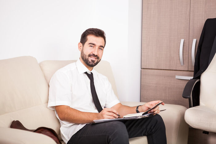 Man in white shirt and black tie sitting on sofa writing notes about disturbing creepy things told to people