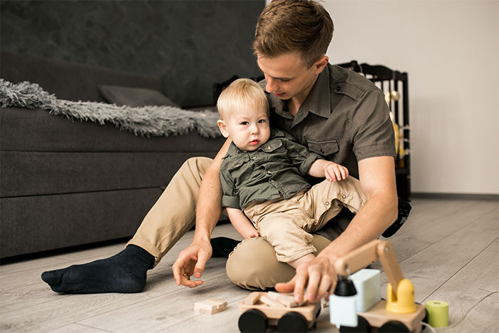 Young father playing with toddler son on floor, symbolizing woman expects help from ex-husband after leaving him for another man. Young father playing with toddler son on floor, symbolizing woman expects help from ex-husband after leaving him for another man.