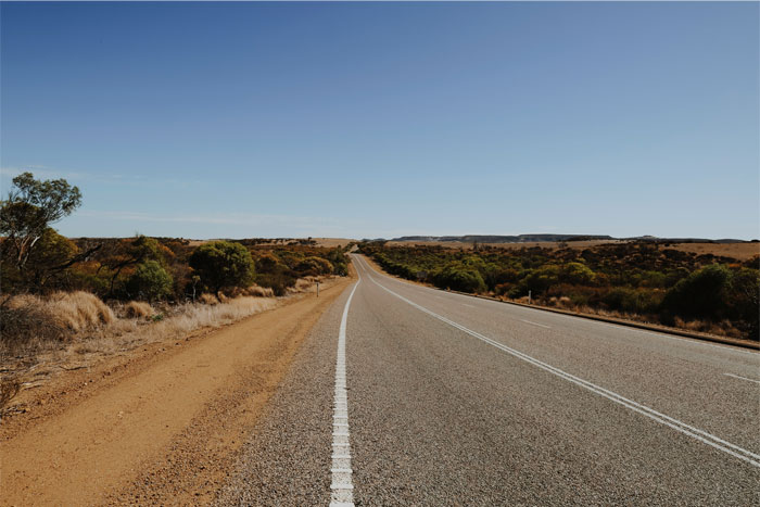 Empty rural road stretching through dry landscape under clear blue sky, related to insurance coverage denial incident. Empty rural road stretching through dry landscape under clear blue sky, related to insurance coverage denial incident.
