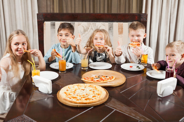 Five kids eating pizza and drinking juice at a restaurant table, illustrating tales from restaurant staff when the bill comes.