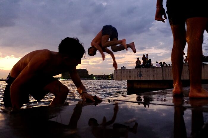 Young men enjoying life on Istanbul’s streets at sunset, with a boy mid-flip near the water’s edge.
