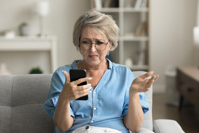 Middle-aged woman struggling with smartphone.