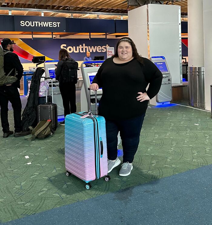 Plus-size activist standing in airport terminal with pastel luggage near Southwest Airlines check-in kiosks. Plus-size activist standing in airport terminal with pastel luggage near Southwest Airlines check-in kiosks.