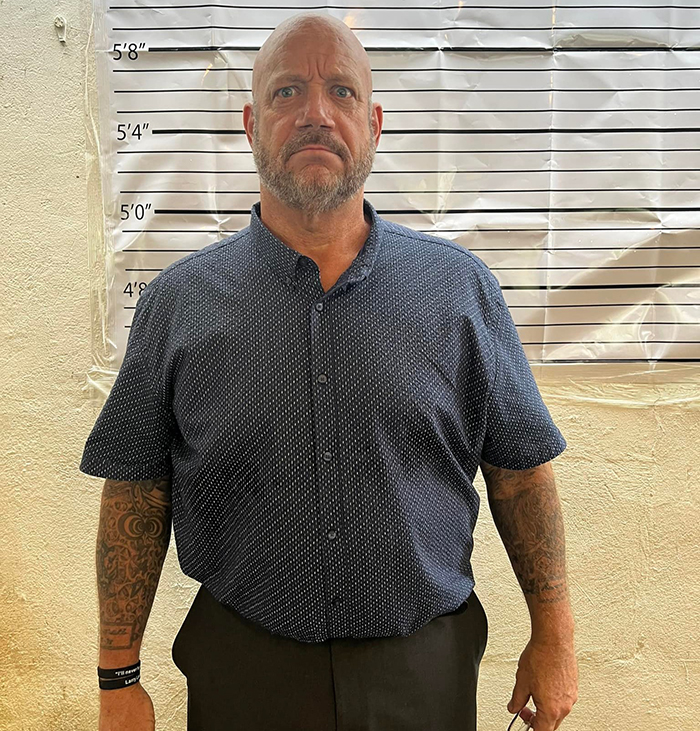 Middle-aged man with tattoos stands in front of height chart, representing America’s most notorious jewel thief. Middle-aged man with tattoos stands in front of height chart, representing America’s most notorious jewel thief.