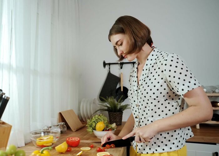 Woman chopping vegetables in kitchen illustrating genius life hacks that trick people into doing extra work.