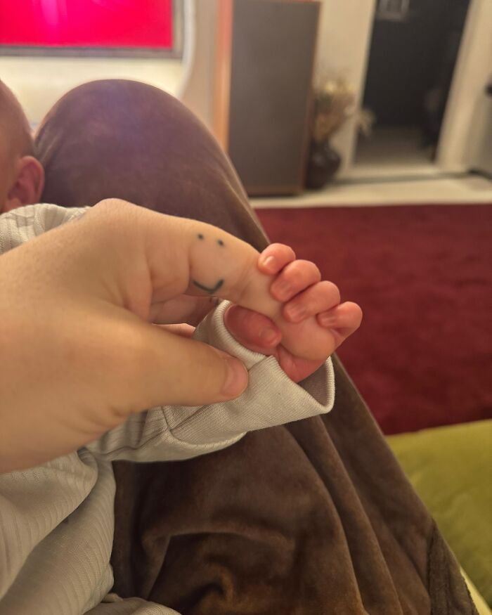 Adult hand with smiley face tattoo holding newborn baby's hand, illustrating pop star naming son related to diabetes news. Adult hand with smiley face tattoo holding newborn baby's hand, illustrating pop star naming son related to diabetes news.