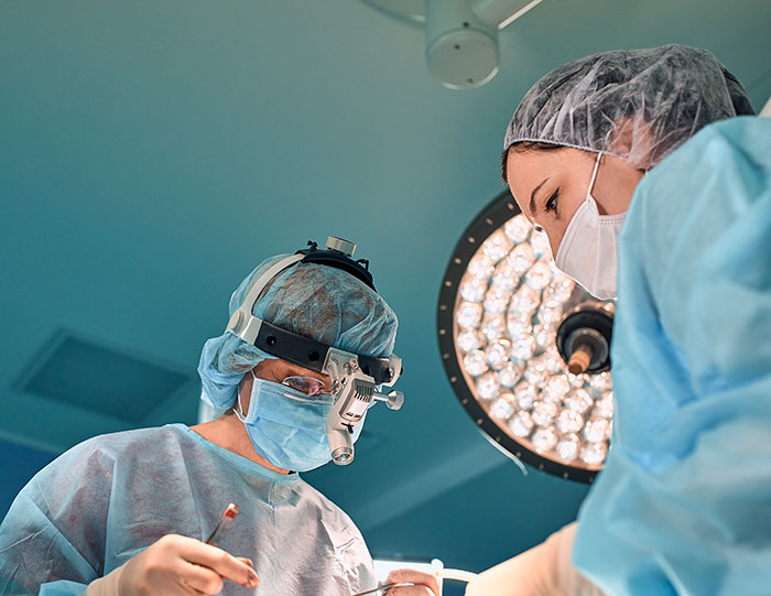 Brain surgeon and assistant performing delicate operation under surgical lights in a sterile operating room. Brain surgeon and assistant performing delicate operation under surgical lights in a sterile operating room.