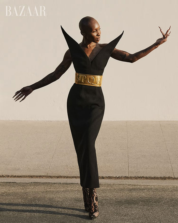 Cynthia Erivo posing in a sculptural black dress with a gold belt, striking an expressive pose in a high-fashion shoot. Cynthia Erivo posing in a sculptural black dress with a gold belt, striking an expressive pose in a high-fashion shoot.