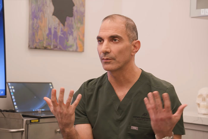 Doctor in green scrubs explaining urgent medical concerns about man with 4-lb face tumor in clinical setting. Doctor in green scrubs explaining urgent medical concerns about man with 4-lb face tumor in clinical setting.