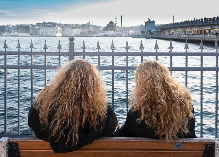 Two women with curly hair sitting on a bench overlooking Istanbul’s streets and waterfront with a cityscape in the background.