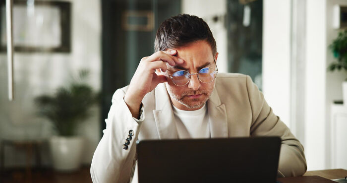 Man with glasses looking confused at laptop screen, illustrating parents being bad at technology skills in a funny way.