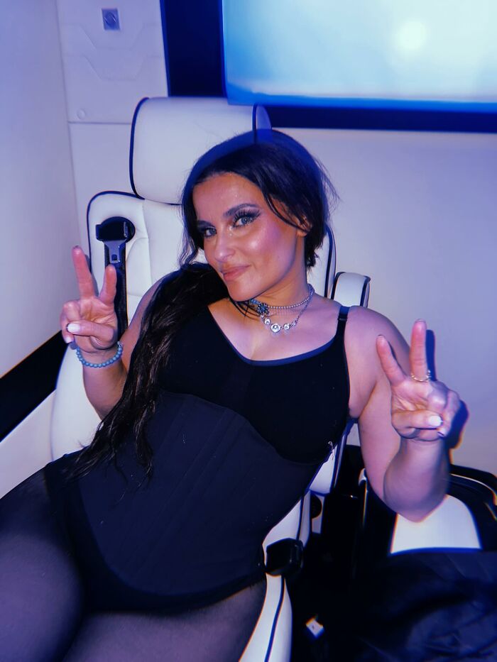 Nelly Furtado seated in a chair, wearing black outfit and jewelry, flashing peace signs with both hands in a relaxed pose. Nelly Furtado seated in a chair, wearing black outfit and jewelry, flashing peace signs with both hands in a relaxed pose.
