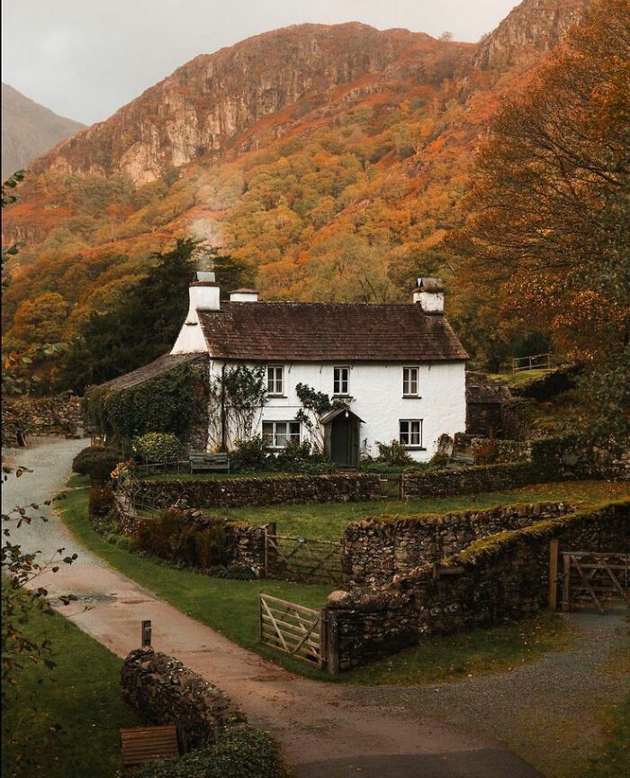 Cozy cottage surrounded by autumn gardens and stone walls with colorful trees on hillside in a peaceful rural setting