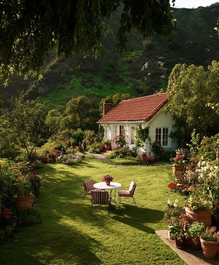 Idyllic dream cottage surrounded by lush gardens and greenery with outdoor table and chairs on a sunny day.