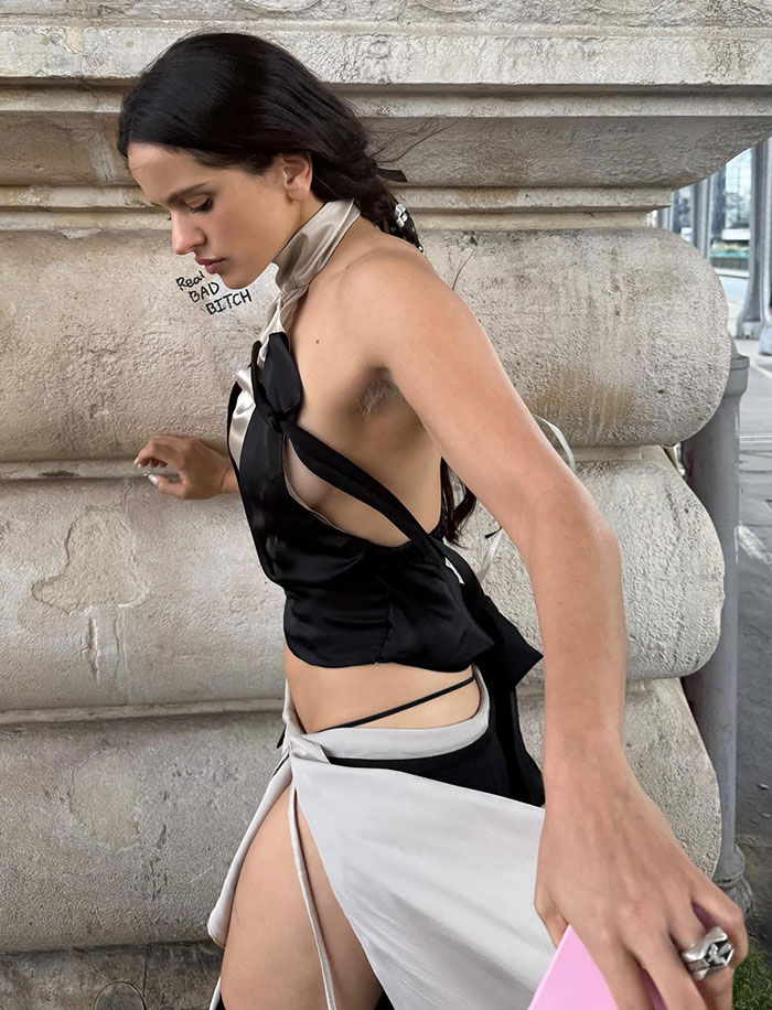 Pop star showing dyed armpit hair at Paris Fashion Week, wearing black and white outfit against stone backdrop. Pop star showing dyed armpit hair at Paris Fashion Week, wearing black and white outfit against stone backdrop.