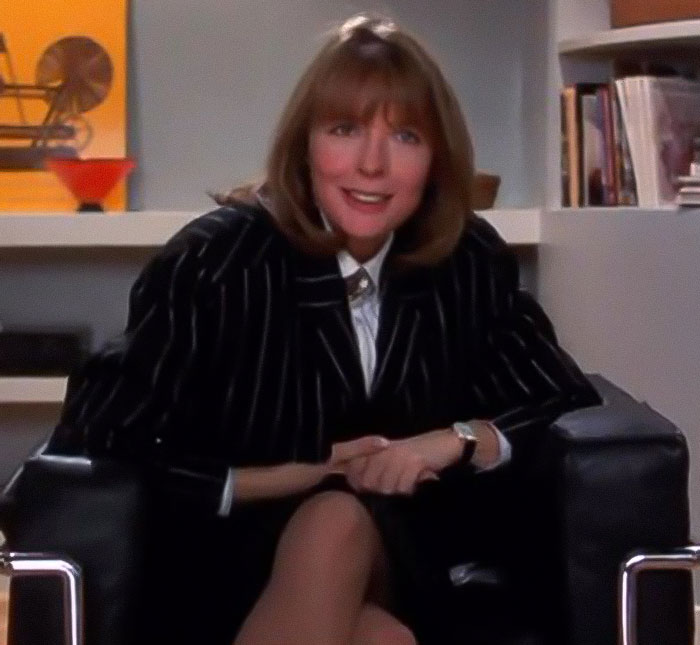 Woman in a pinstripe blazer sitting on a black chair, smiling during an indoor interview setting. Woman in a pinstripe blazer sitting on a black chair, smiling during an indoor interview setting.