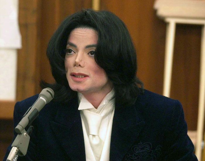 Michael Jackson speaking at a press conference wearing a dark suit with long black hair and white shirt. Michael Jackson speaking at a press conference wearing a dark suit with long black hair and white shirt.